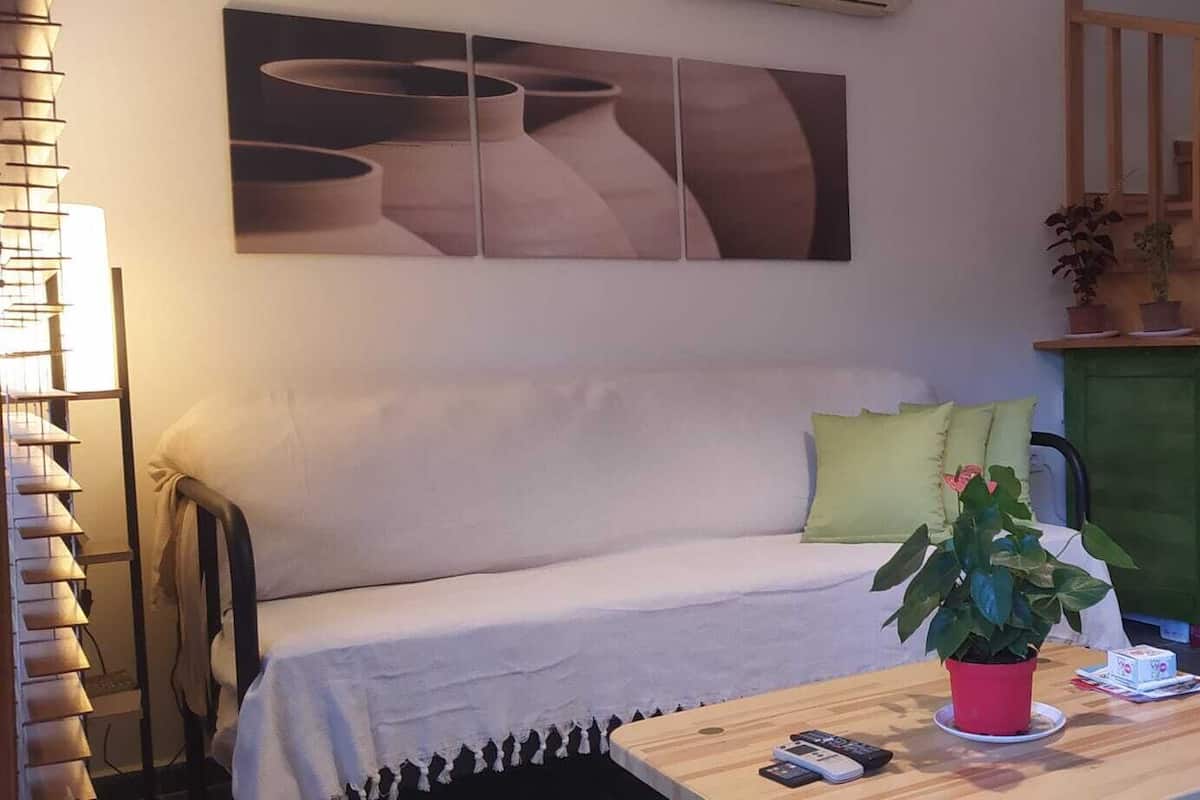 A living room with a sofa, a coffee table with a plant, a staircase, and a wall with abstract art.