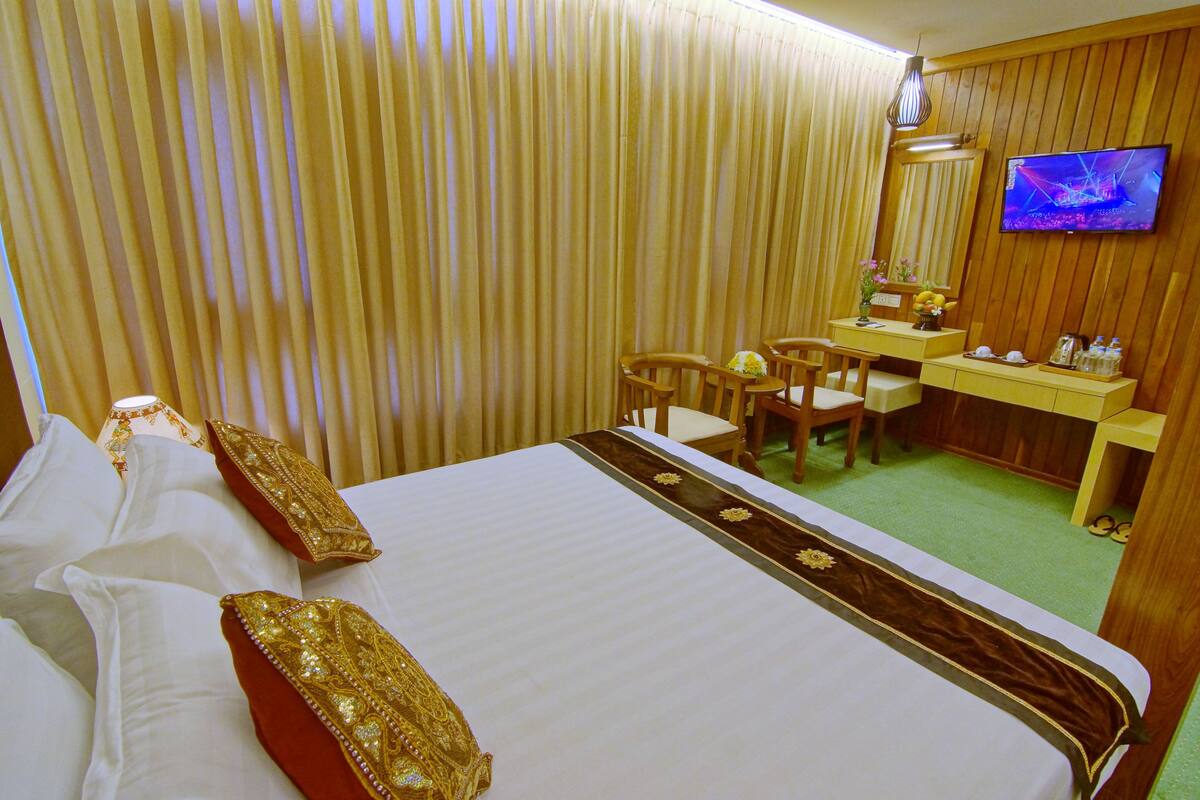 Ein Hotelzimmer mit einem großen Bett, einem Schreibtisch, einem Stuhl, einem Fernseher und einem Spiegel.