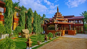 A traditional building with a multi-tiered roof, surrounded by lush greenery and palm trees. - Hotel Yadanarbon Bagan (Nyaung-U)