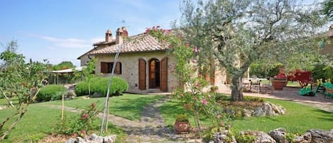 A stone house with a tiled roof, a small garden with a pathway, and a tree with pink flowers.