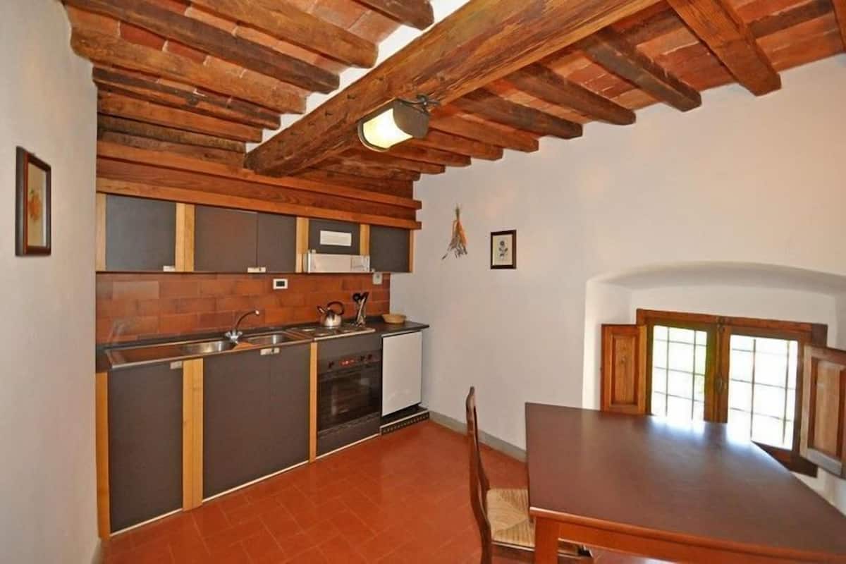 A compact kitchen with a wooden ceiling, a built-in stove, and a dining area with a large table and chairs.