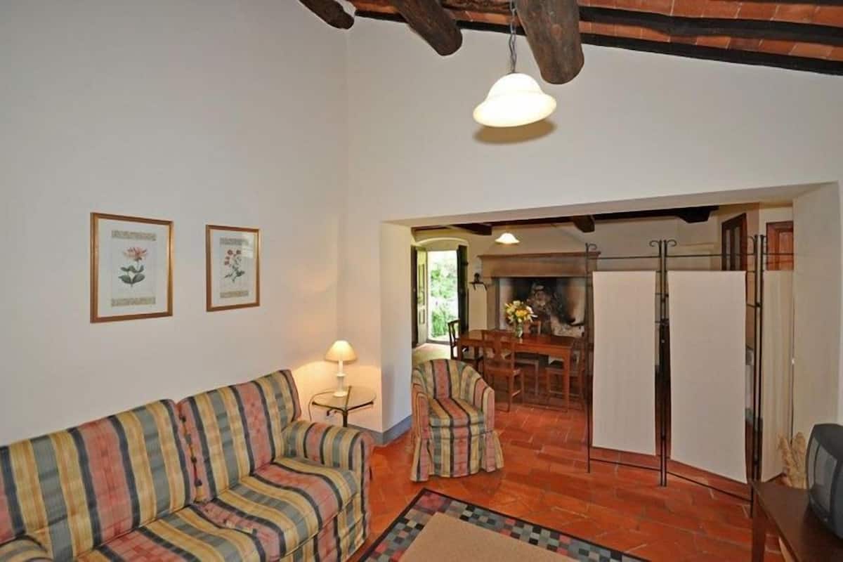 A living room with a striped sofa, a small table with a lamp, and a dining area with chairs and a table.