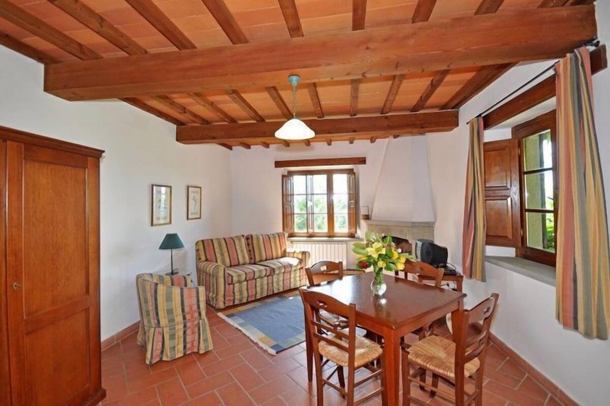 A cozy living room with a wooden ceiling, a striped sofa, a dining table with chairs, and a window with curtains.