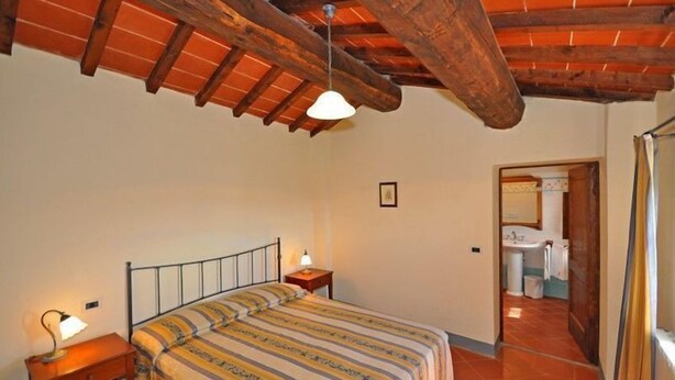 A bedroom with a wooden ceiling, a bed with striped bedding, a bedside lamp, and a small bedside table. - Civetta (Capolona)