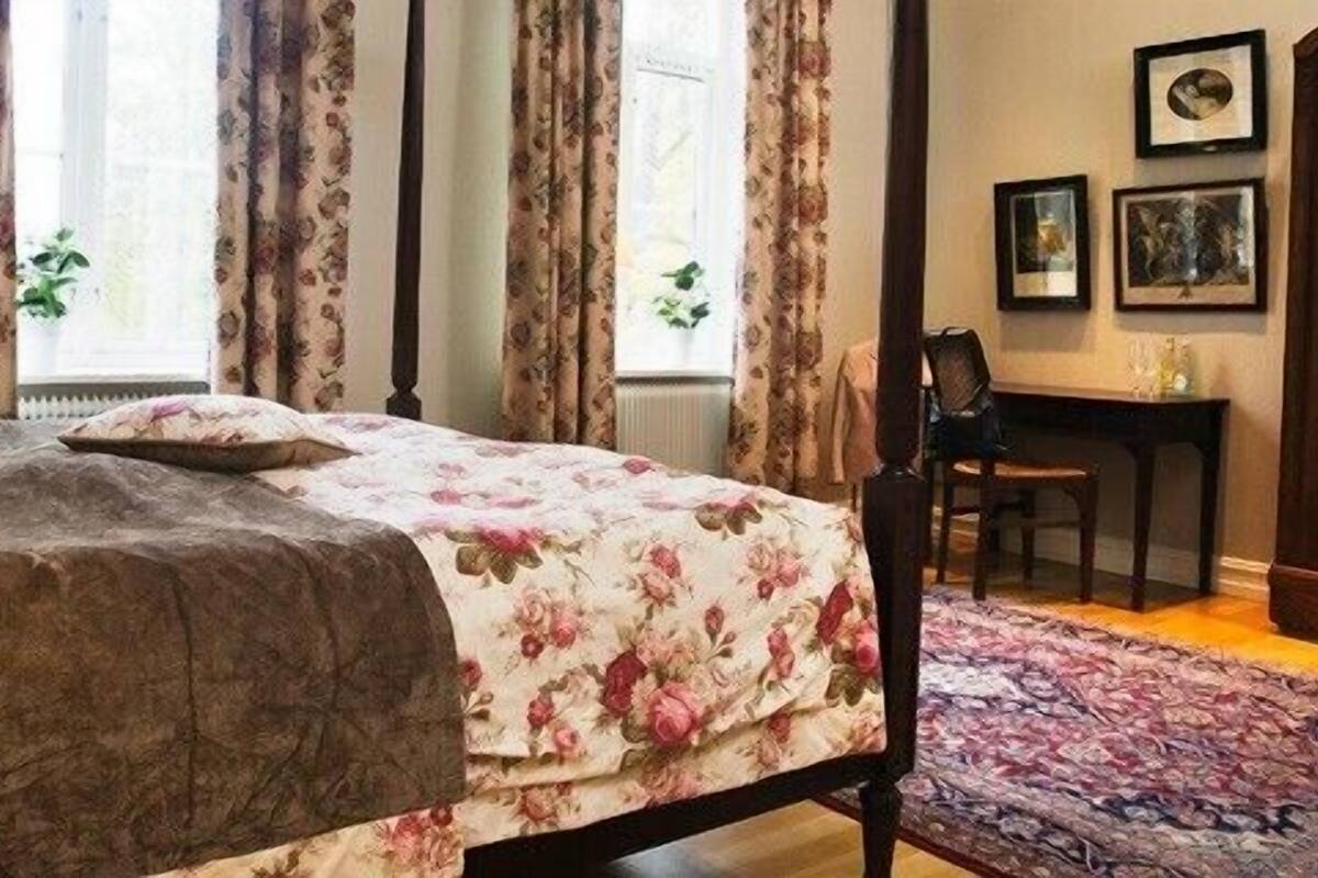 Un dormitorio con cama, escritorio, silla, espejo y ventana con cortinas.