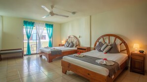 A hotel room with two wooden beds, a bench, a ceiling fan, and a balcony with curtains. - Hotel Plaza Europa (Sosúa)