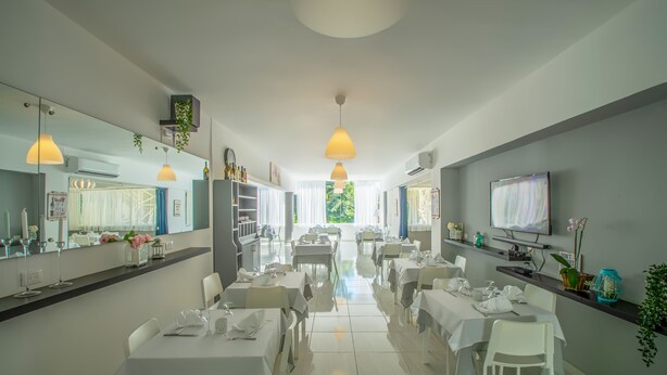 A modern dining area with white tables and chairs, pendant lighting, and a TV on the wall. - Hotel Plaza Europa (Sosúa)