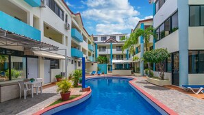 A swimming pool surrounded by a multi-story building with balconies, outdoor seating, and potted plants. - Hotel Plaza Europa (Sosúa)