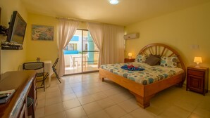 A bedroom with a wooden bed, a desk, a chair, a TV, and a balcony with a table and chairs. - Hotel Plaza Europa (Sosúa)