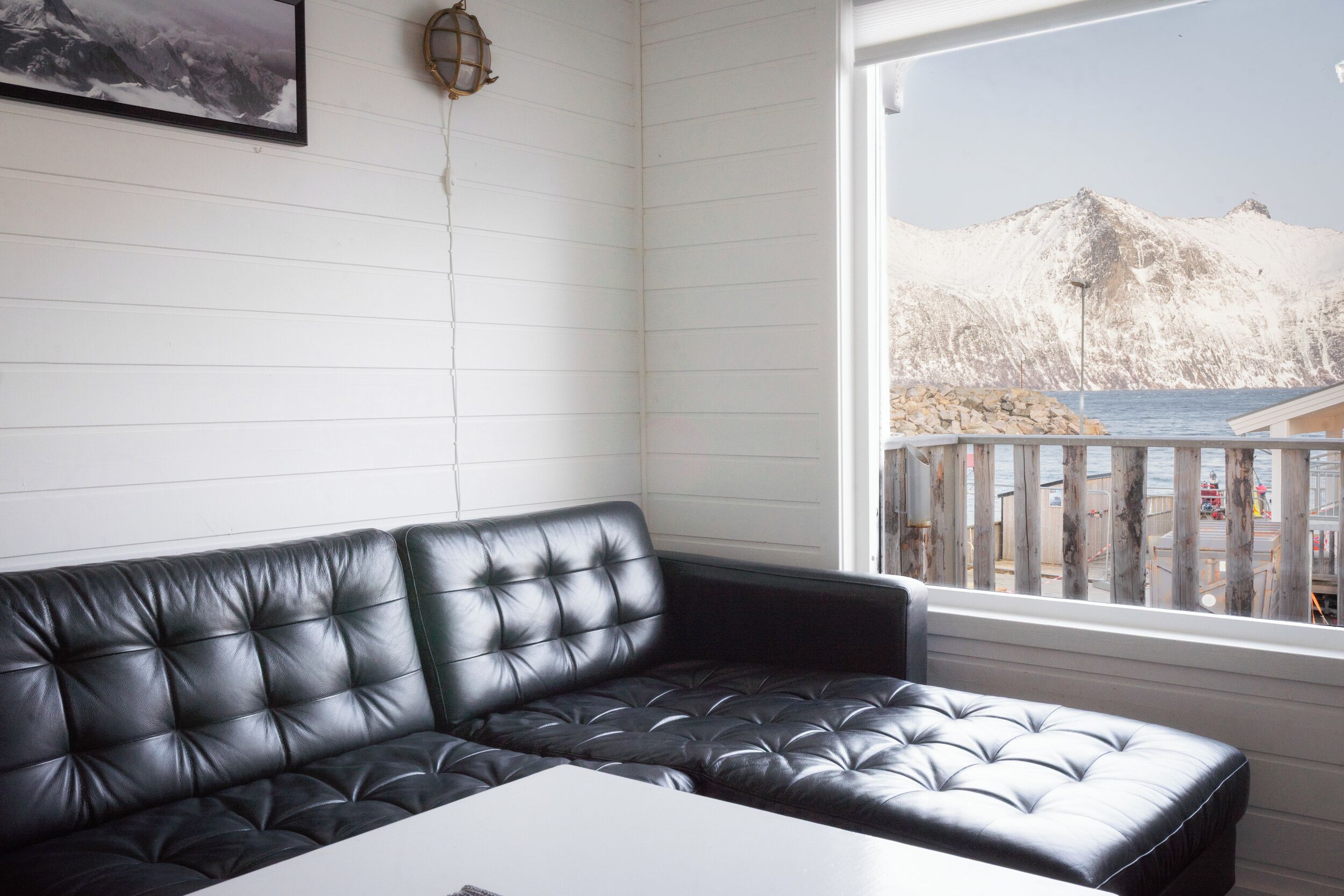 A black leather sofa in a room with a white wall and a window overlooking a beach.