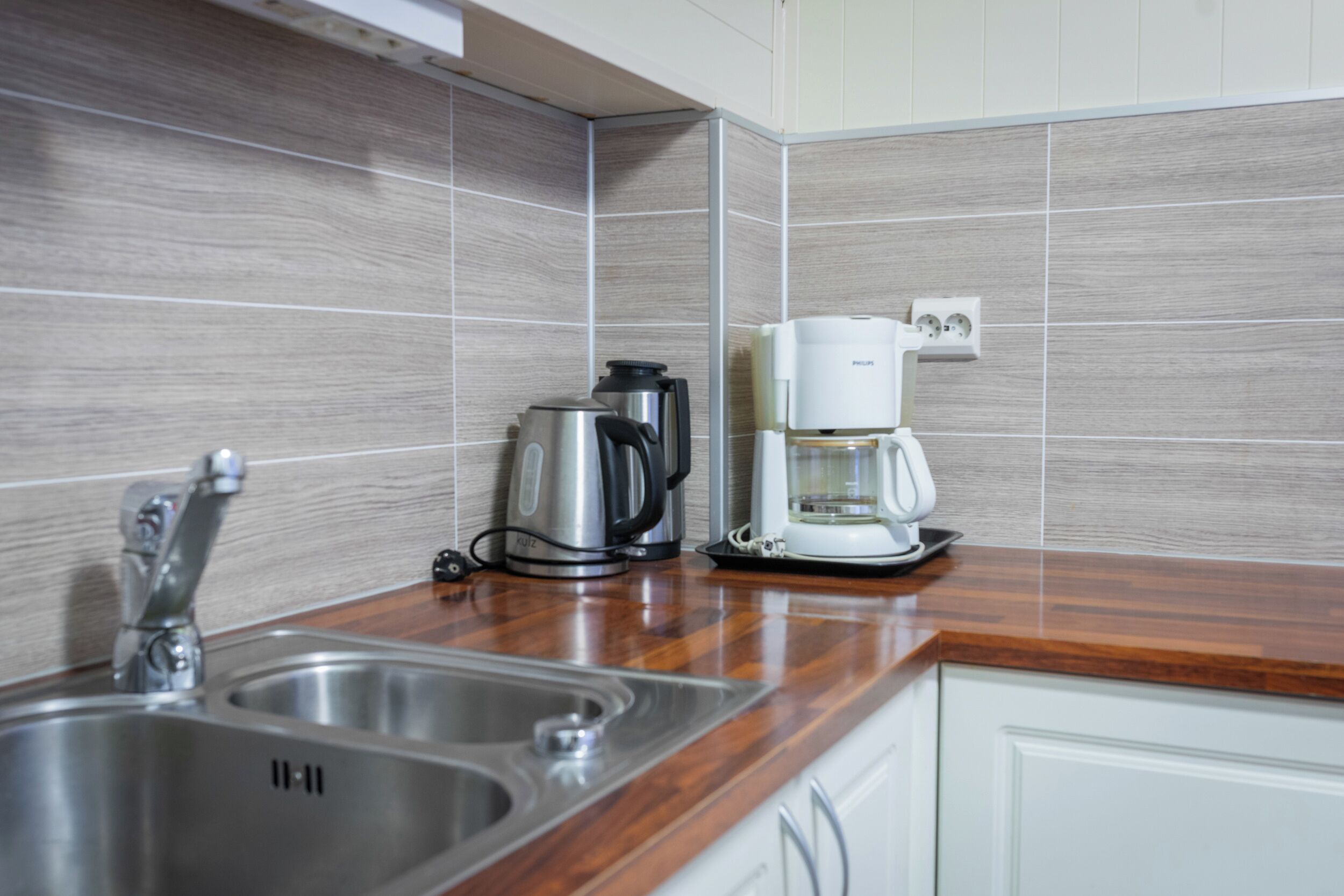 Una cocina con un lavamanos de acero inoxidable, una cafetera y un hervidor en la encimera.
