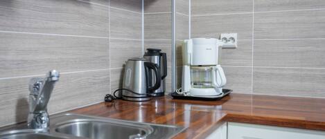 Una cocina con un lavamanos de acero inoxidable, una cafetera y un hervidor en la encimera.