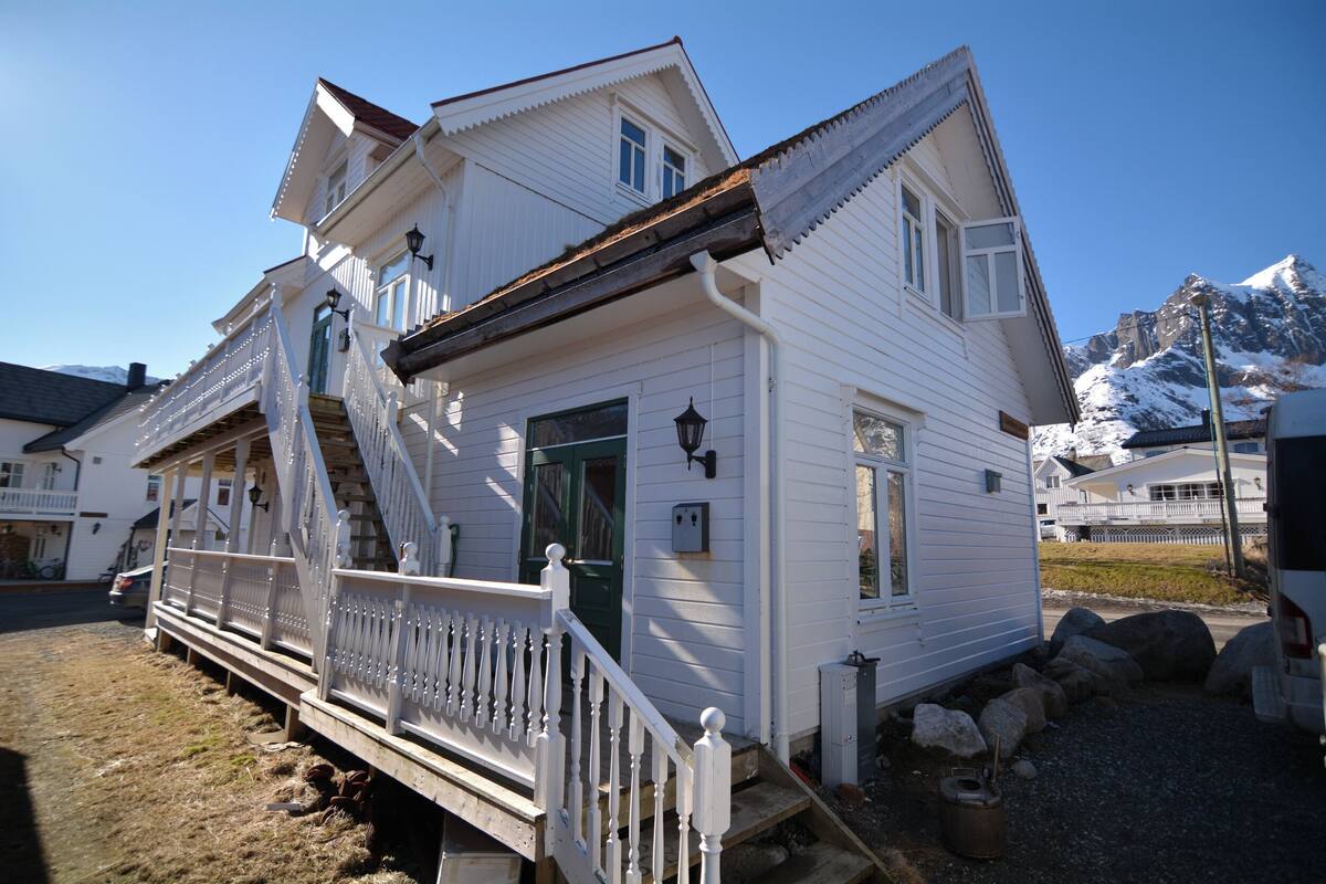 Une maison en bois blanche, avec un escalier, une porte verte et un petit porche.
