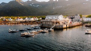 Un pueblo costero con un edificio blanco destacado, barcos amarrados y montañas al fondo.