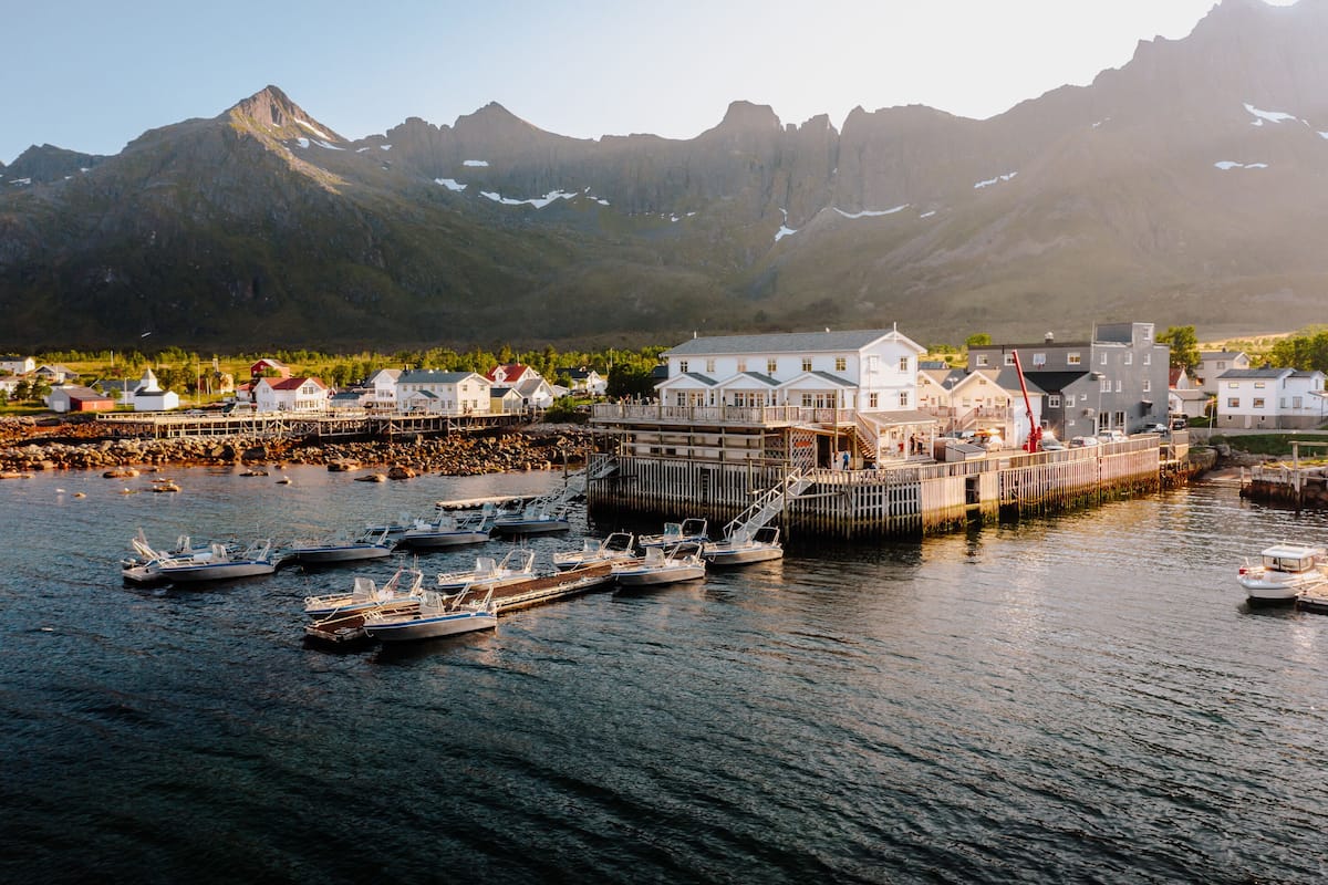 Une ville côtière avec un imposant bâtiment blanc, des bateaux amarrés et des montagnes en arrière-plan.