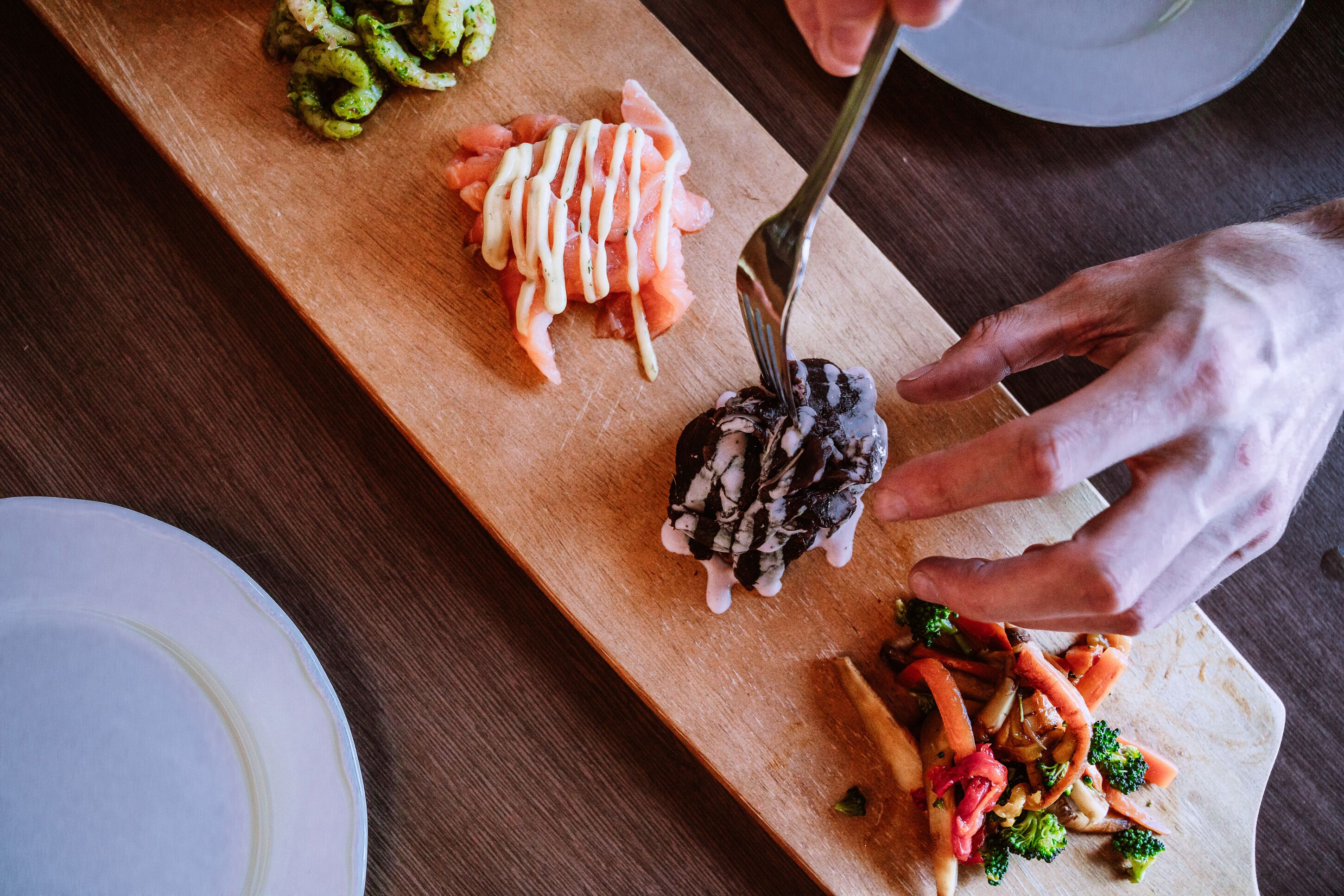 A wooden board with various food items, including sliced salmon, a dark-colored vegetable, and stir-fried vegetables.