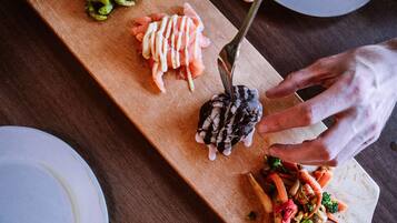 A wooden board with various food items, including sliced salmon, a dark-colored vegetable, and stir-fried vegetables.
