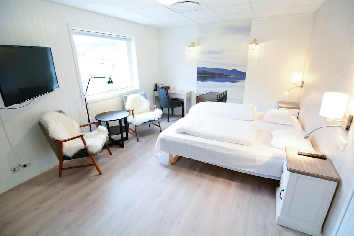 Une chambre d’hôtel avec un lit, un bureau, une chaise, une télévision et un tableau représentant un lac.