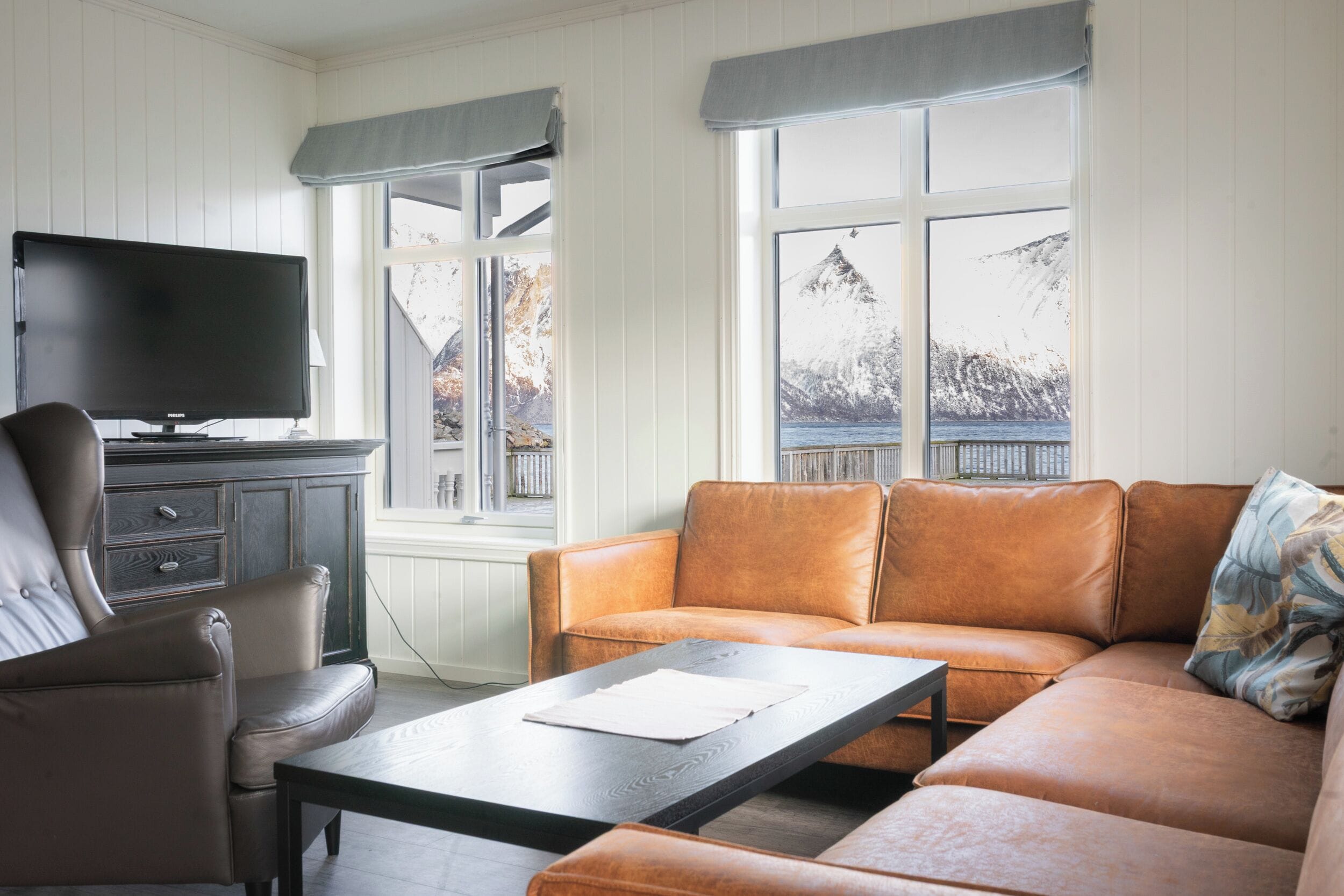 A living room with a brown leather sofa, a black coffee table, a brown leather armchair, and a flat-screen TV on a cabinet.