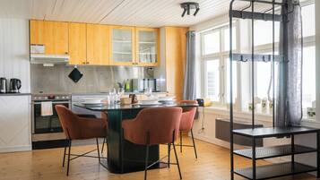 Una cocina moderna con armarios de madera, una isla central con sillas, un estante de metal negro y una ventana con cortinas.