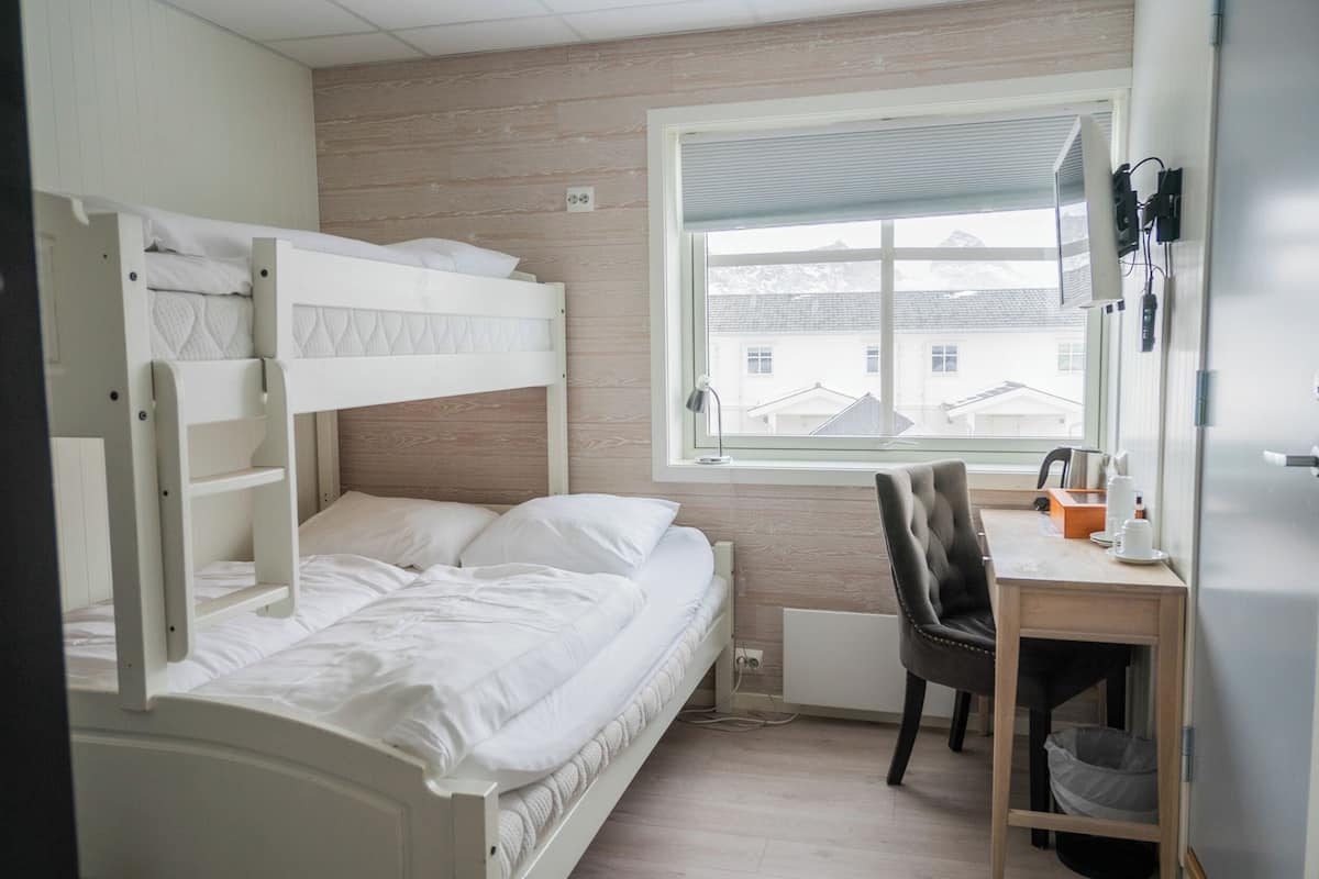 Un lit superposé avec une literie blanche, un bureau avec une chaise et une fenêtre donnant sur des immeubles.