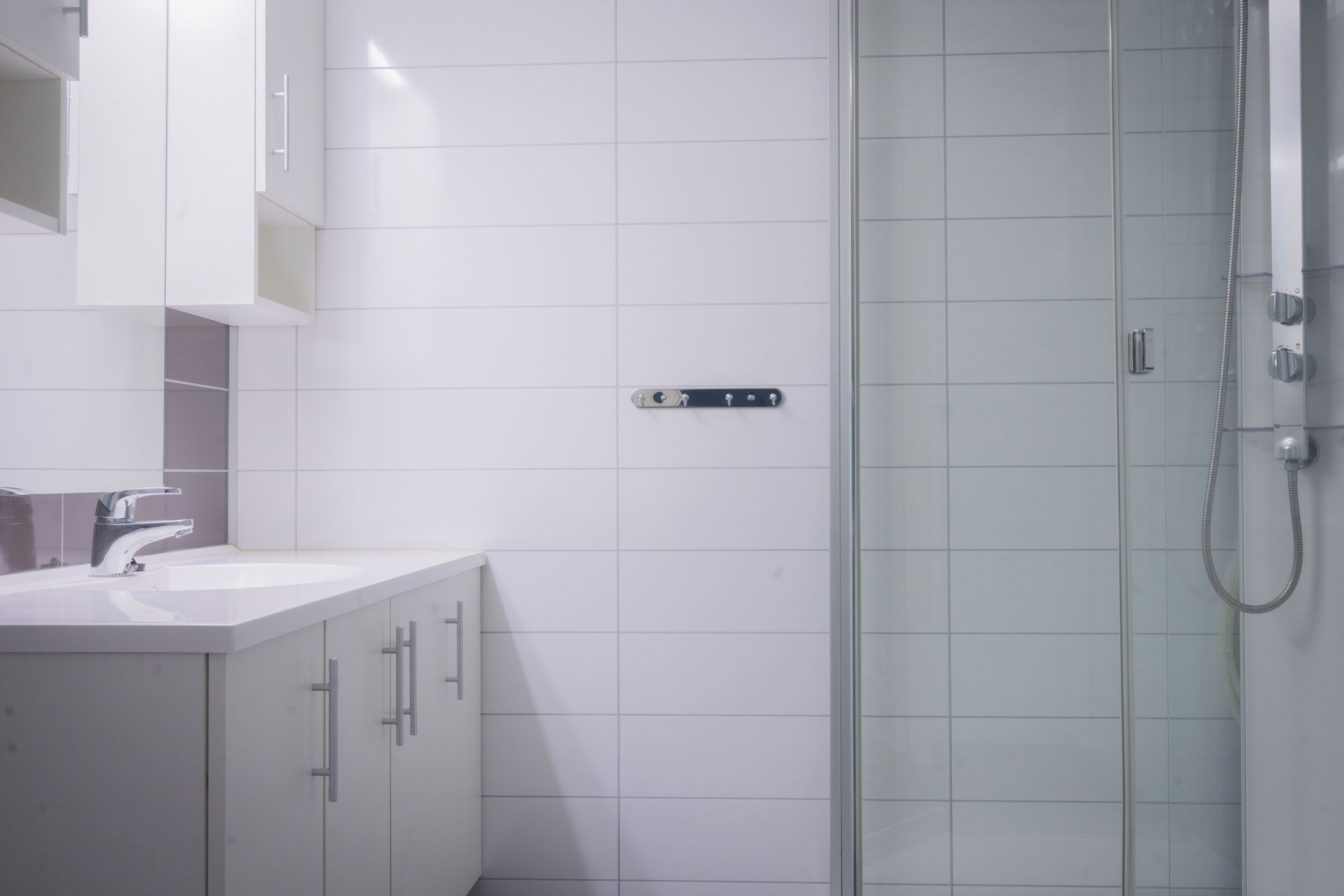 Une salle de bain moderne avec un mur recouvert de carreaux blancs, une douche en verre et un lavabo blanc doté d’un robinet.