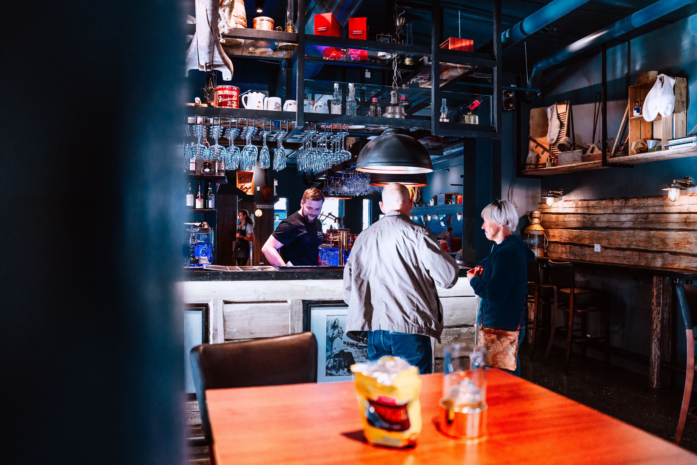 Een bar met glazen en flessen op planken, een houten toonbank en een tafel met een drankje en een hapje.