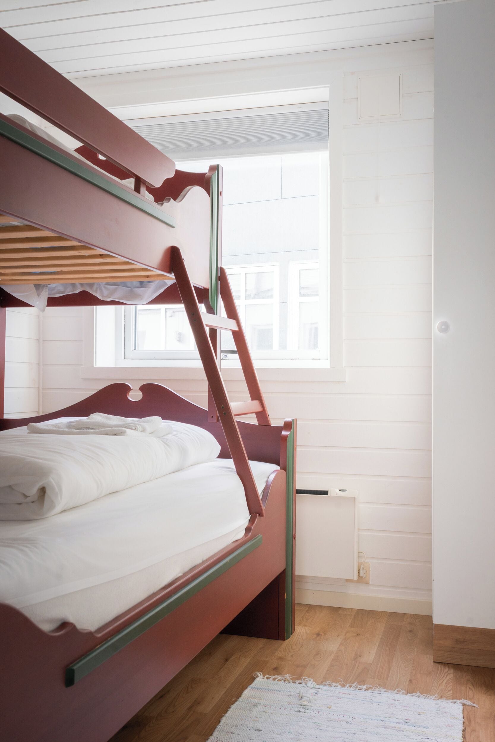 Una cama litera con escalera, ropa de cama blanca y una ventana con persianas.