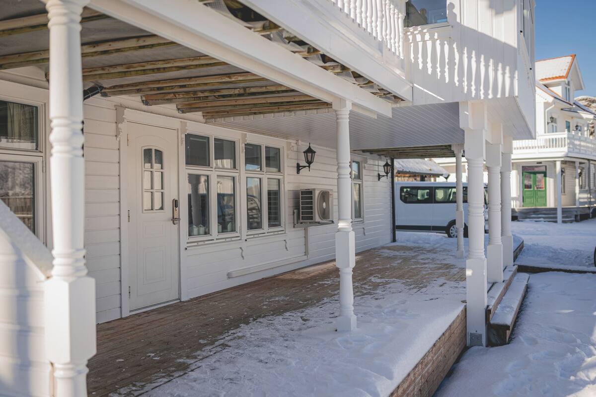 Un bâtiment blanc doté d’un porche abrité et d’une terrasse en bois.