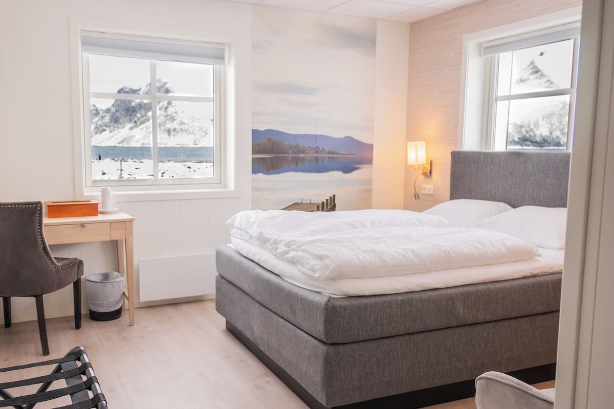 Une chambre à coucher avec un lit, un bureau, une chaise et une vue sur les montagnes par la fenêtre.