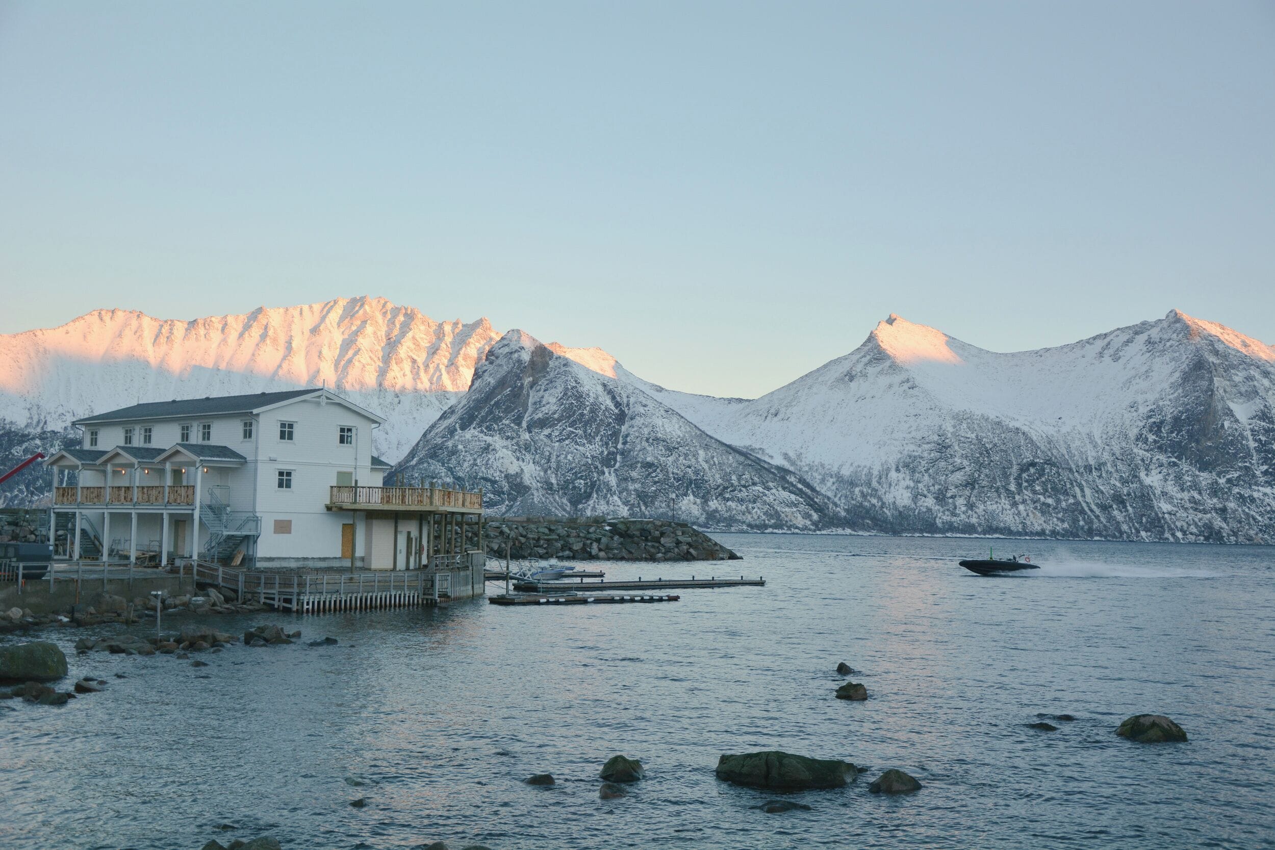 Un bâtiment situé sur la côte, doté d’un quai s’étendant dans des eaux calmes, et entouré de montagnes enneigées.