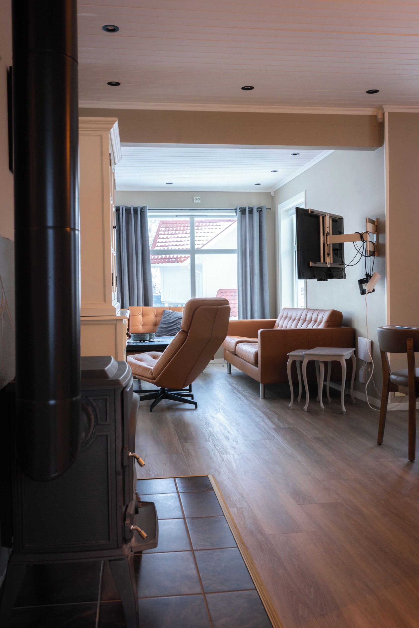 Een woonkamer met een open haard, een bank, een fauteuil en een aan de muur bevestigde televisie.