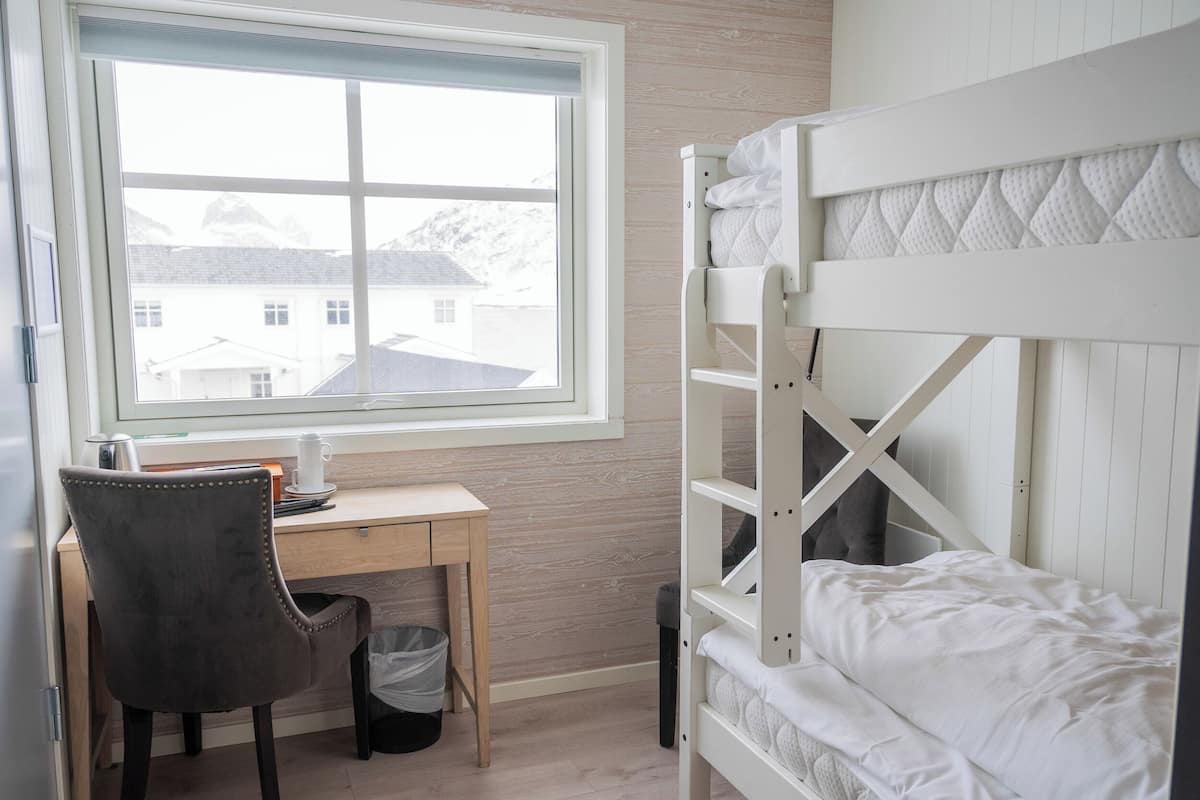 Un lit superposé avec une fenêtre, un bureau avec une chaise et une poubelle.