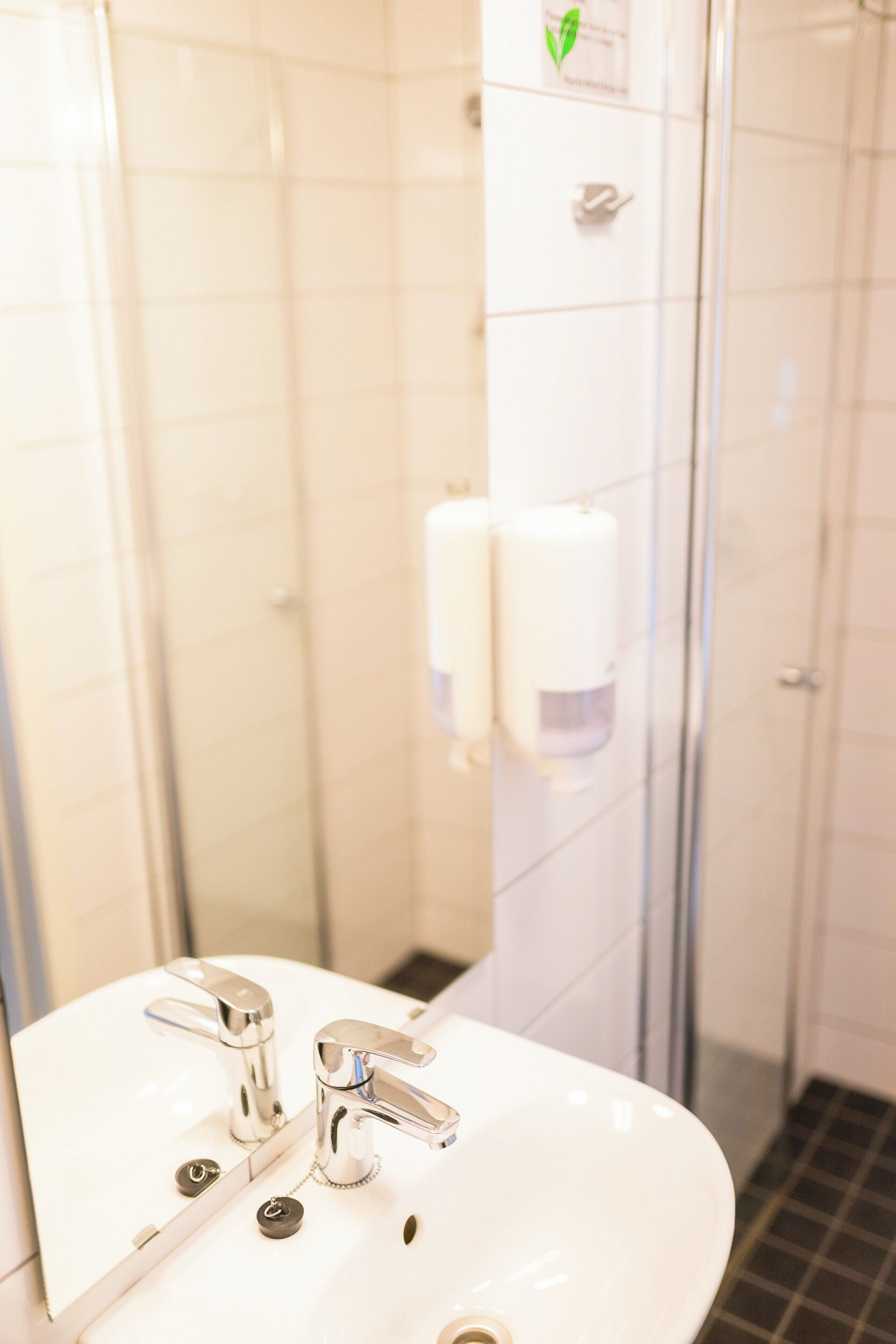 A bathroom with a white sink, two faucets, and a mirror. There are two hand soap dispensers on the wall.