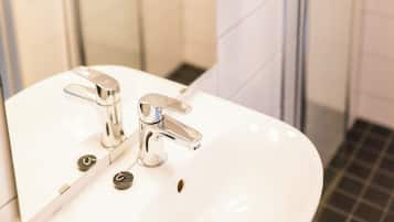 A bathroom with a white sink, two faucets, and a mirror. There are two hand soap dispensers on the wall.