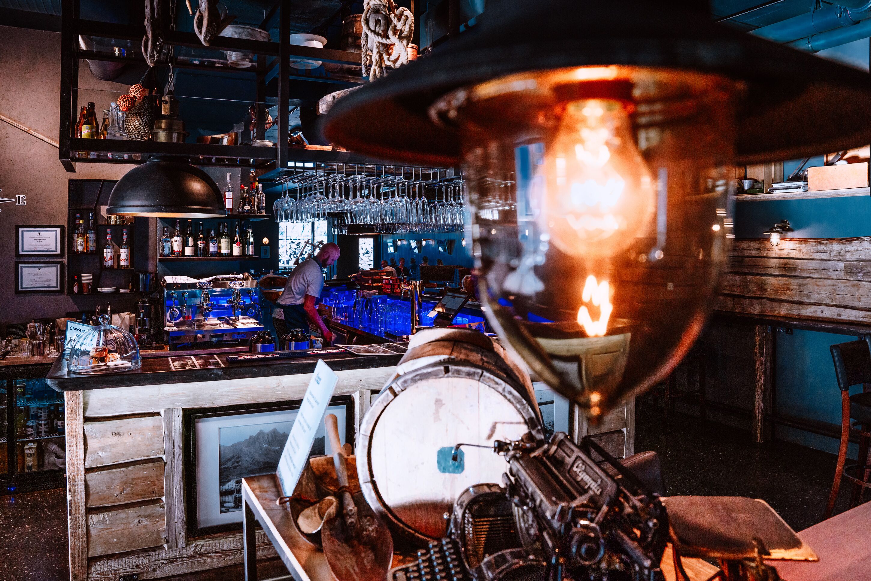 A bar area with a vintage jukebox, shelves of bottles, and a bartender preparing drinks.