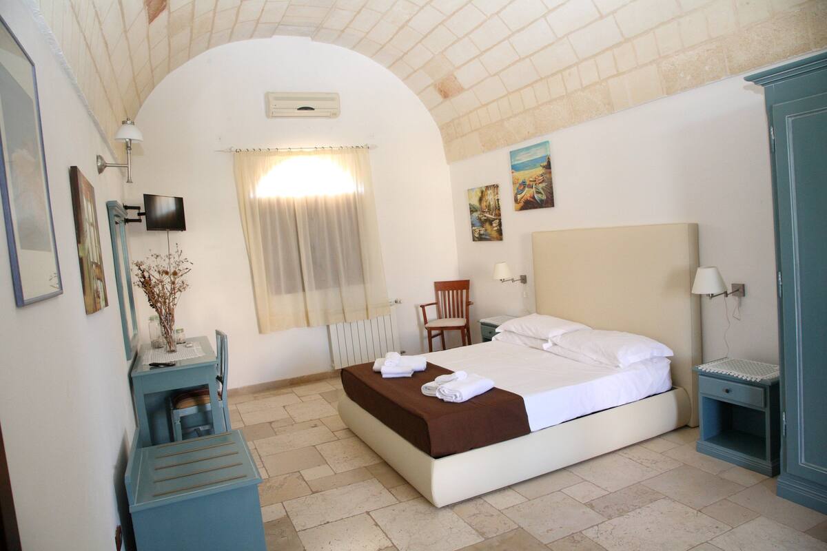 Une chambre à coucher comprenant un lit, un bureau, une chaise, un téléviseur et des œuvres d’art accrochées aux murs.