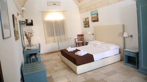 A bedroom with a bed, a desk, a chair, a TV, and artwork on the walls.