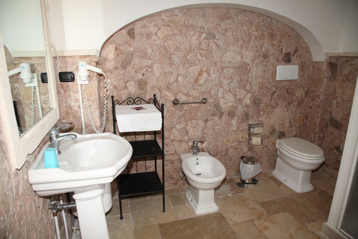 A bathroom with a stone wall, a sink, a bidet, and a toilet.