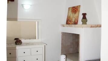 Een kamer met een witte boogdoorgang, een witte tafel met een vaas en kaarsen, een geruit stoel, en een open haard met een schilderij erboven.
