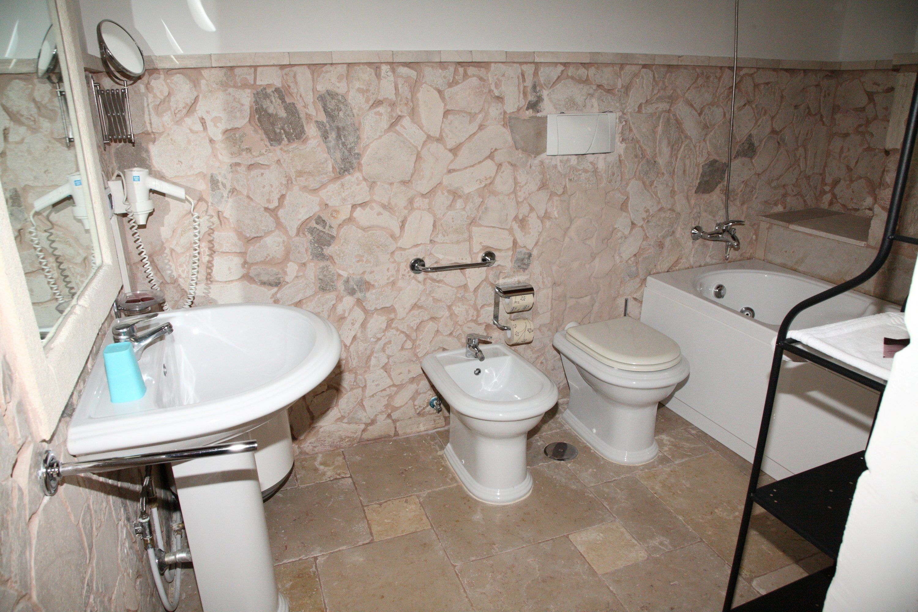 A bathroom with a stone wall, a sink, a bidet, a toilet, and a bathtub.