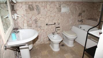 A bathroom with a stone wall, a sink, a bidet, a toilet, and a bathtub.