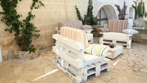 A stone patio with white furniture, including two sofas and a chair, and a brick wall with greenery.