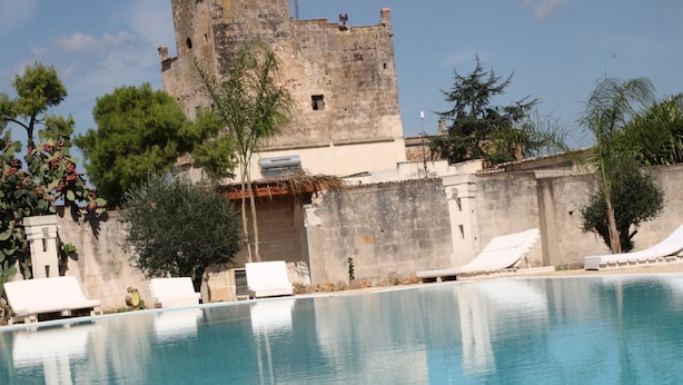 A swimming pool with lounge chairs, a castle-like structure in the background, and some greenery.