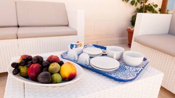 A wicker sofa, a tray with fruits and dishes, and a potted plant in a sunny outdoor setting.