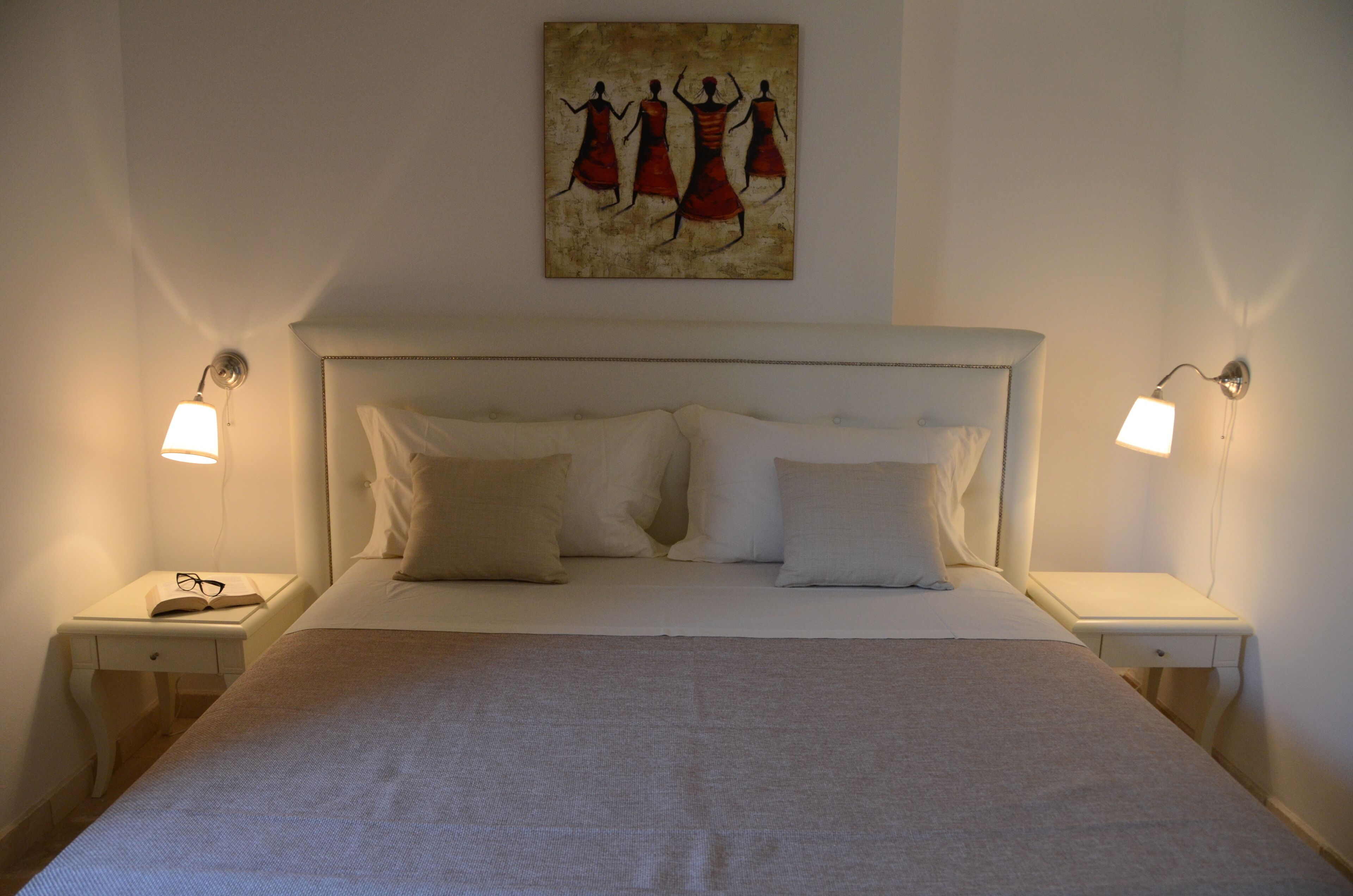 Un lit bien fait, avec une tête de lit, deux tables de chevet avec des lampes et un tableau au-dessus du lit.