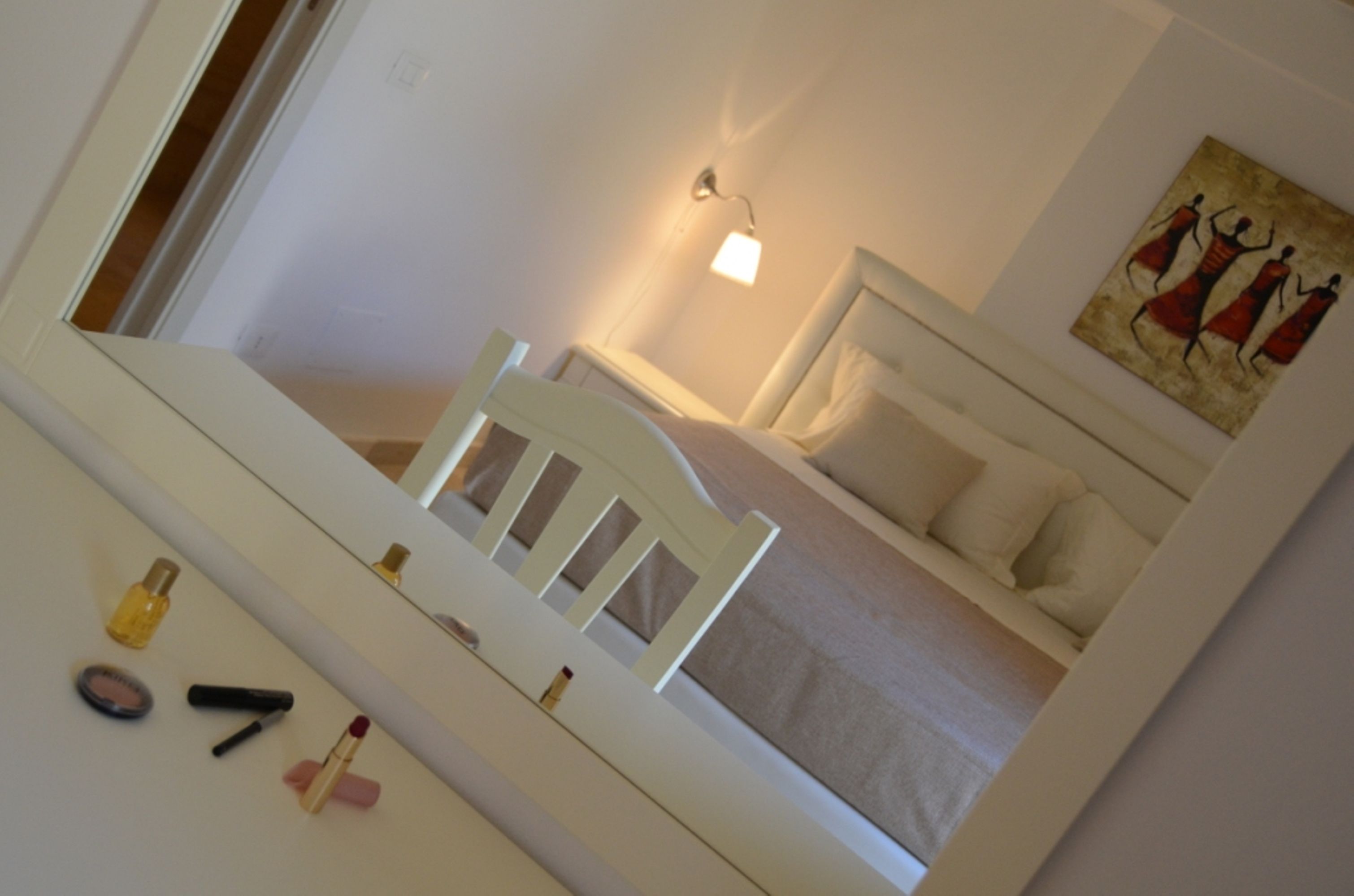 A bedroom with a bed, a nightstand, a mirror, and a painting on the wall.