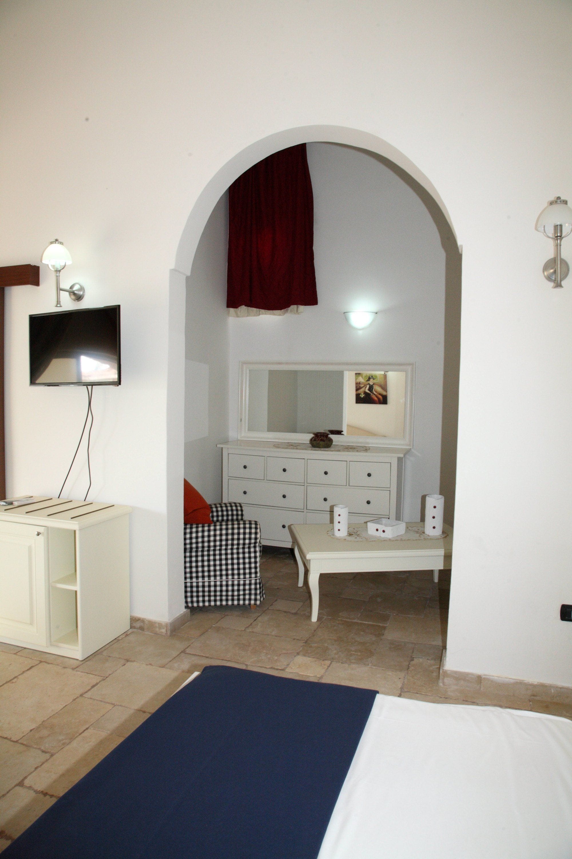 Ein Schlafzimmer mit einem Bett, einem Fernseher, einem Schminktisch, einem Spiegel und einem roten Vorhang.