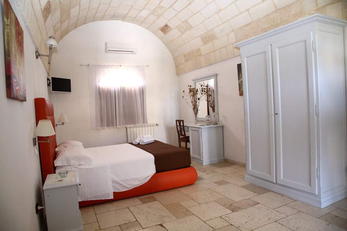 A bedroom with a bed, a desk, a wardrobe, and a TV on the wall.