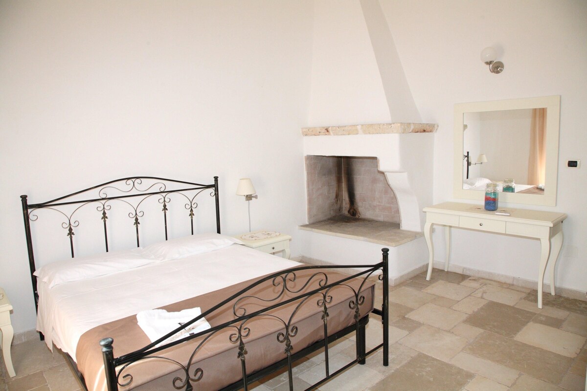 Een slaapkamer met een bed, nachtkastje, kaptafel, dressoir, spiegel en een open haard.